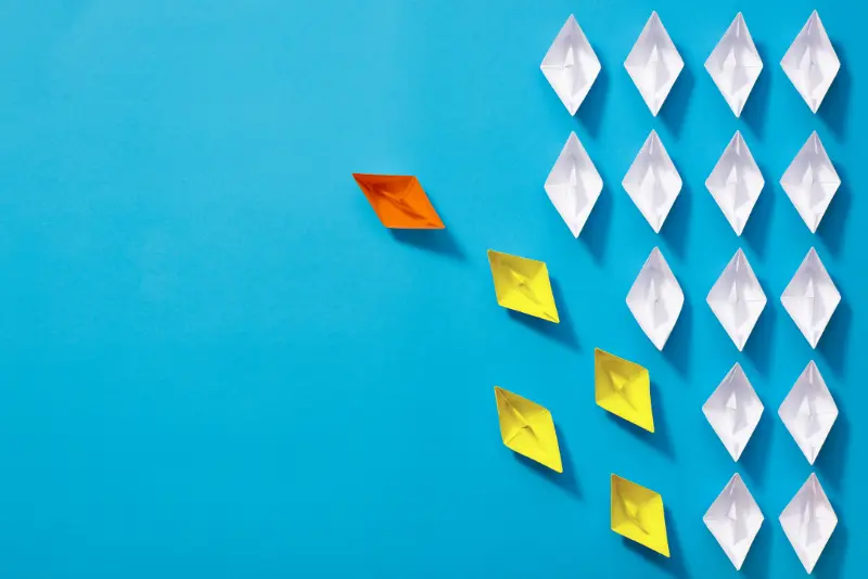 Red paper boat leading a group of white boats – symbolizing leadership, direction, and influence